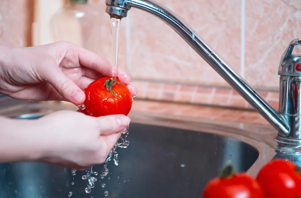 Une personne qui lave une tomate avec une pression adaptée au robinet